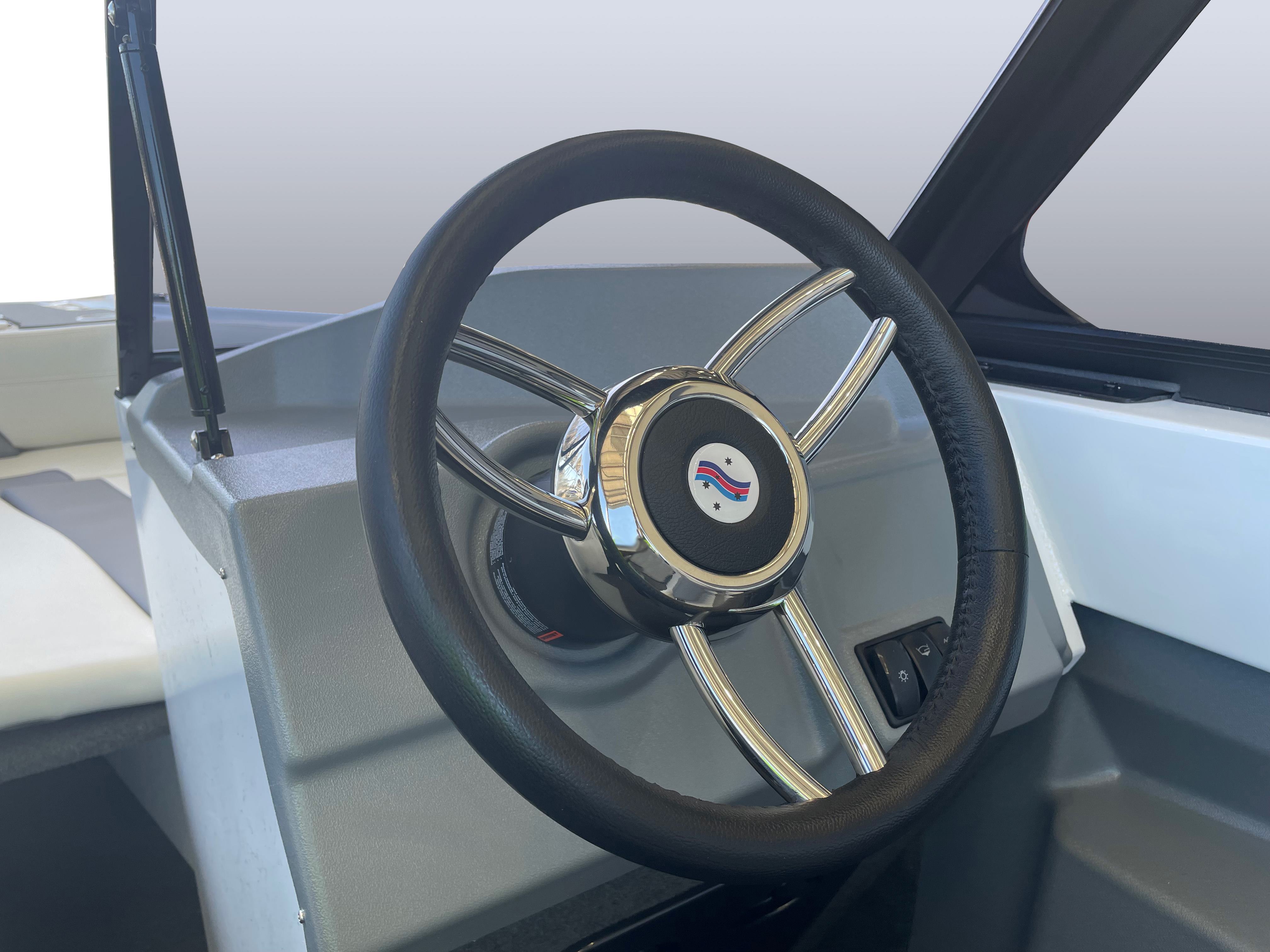 Close-up of a Quintrex boat's steering wheel at the helm, featuring a three-spoke chrome design and a central logo.