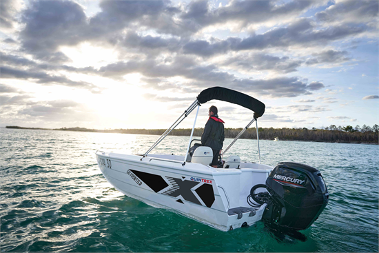 A person driving a Quintrex Frontier on the water at sunset under a cloudy sky, powered by a Mercury outboard motor.