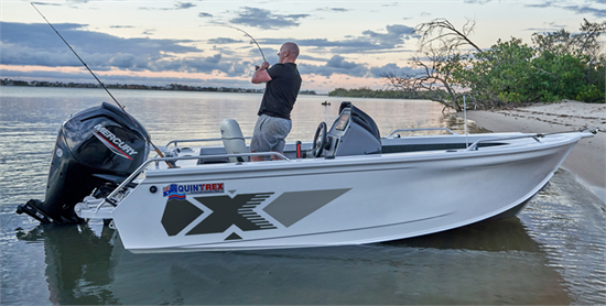 A man fishes from a Quintrex Top Ender boat with a Mercury motor, anchored on a sandy beach at sunset.